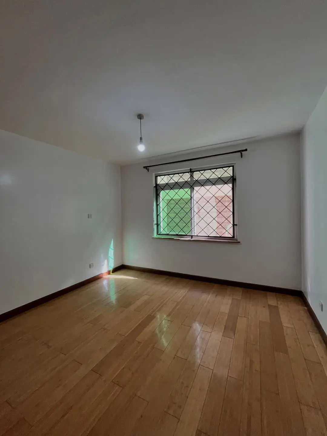 Spacious bedroom with wooden floor and barred window