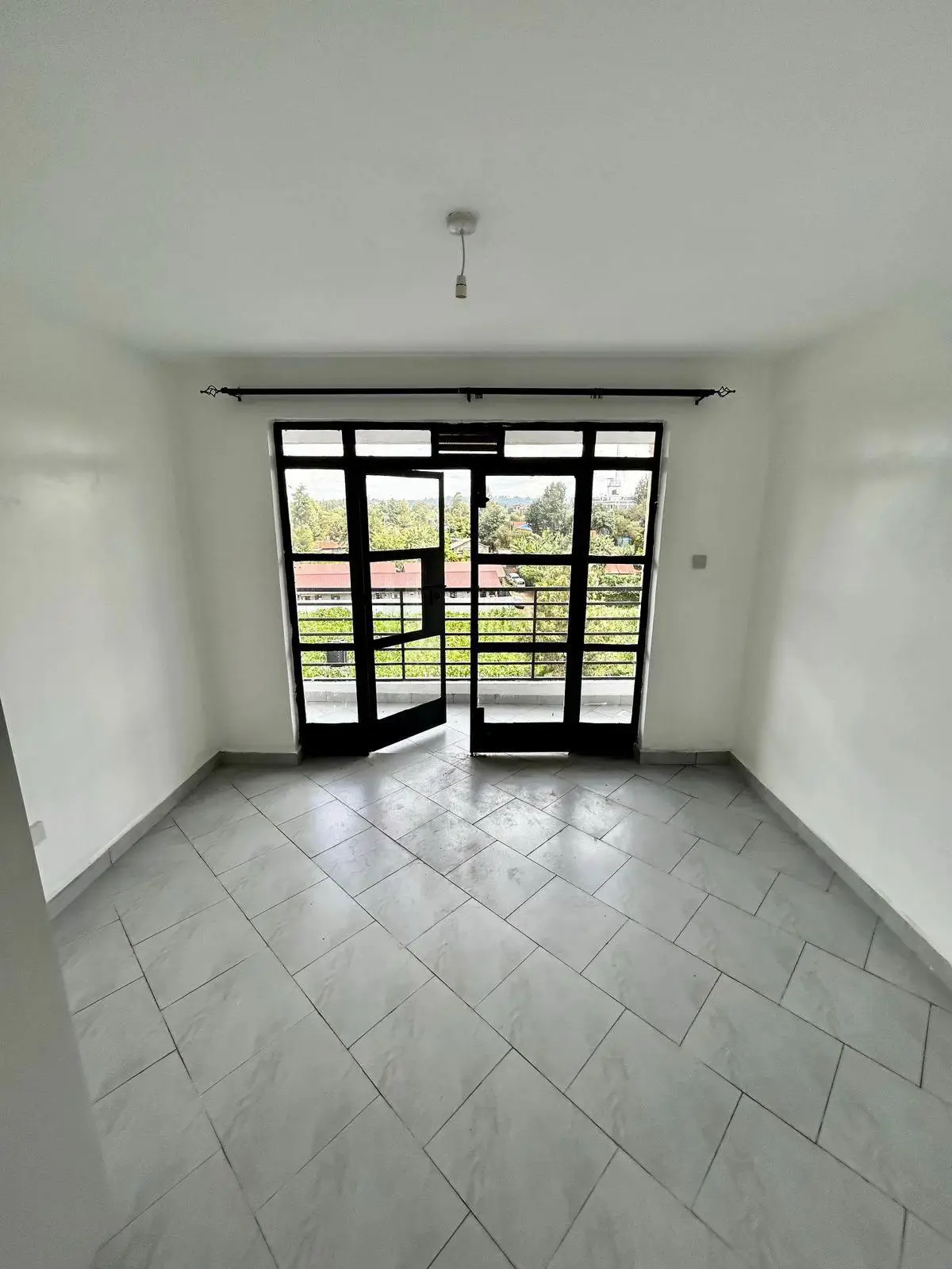 Empty room with black-framed doors leading to a balcony overlooking green landscape